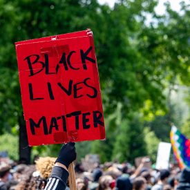 Red sign is held up from a crowd, and it read Black Lives Matter.