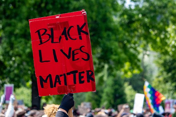 Red sign is held up from a crowd, and it read Black Lives Matter.