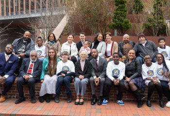 A group of participants at the Trotter 150 anniversary celebration. They are sitting on a brick wall outdoors in Harvard Square. .