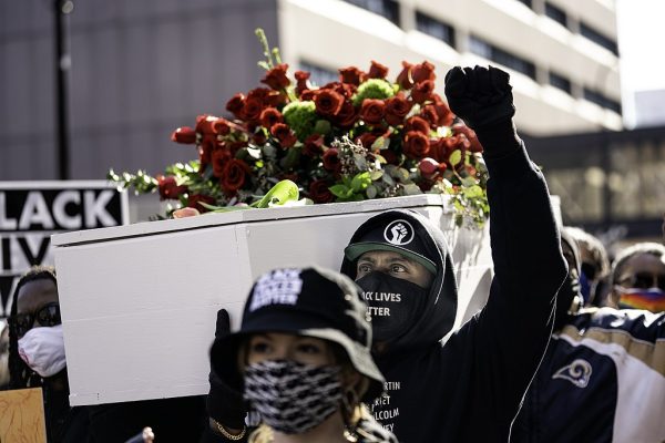 With fist raised, Raj Sethuraju, helps carry a mock coffin during a silent march for justice for George Floyd in downtown Minneapolis, Minnesota on the day before the beginning of the trial of Derek Chauvin.